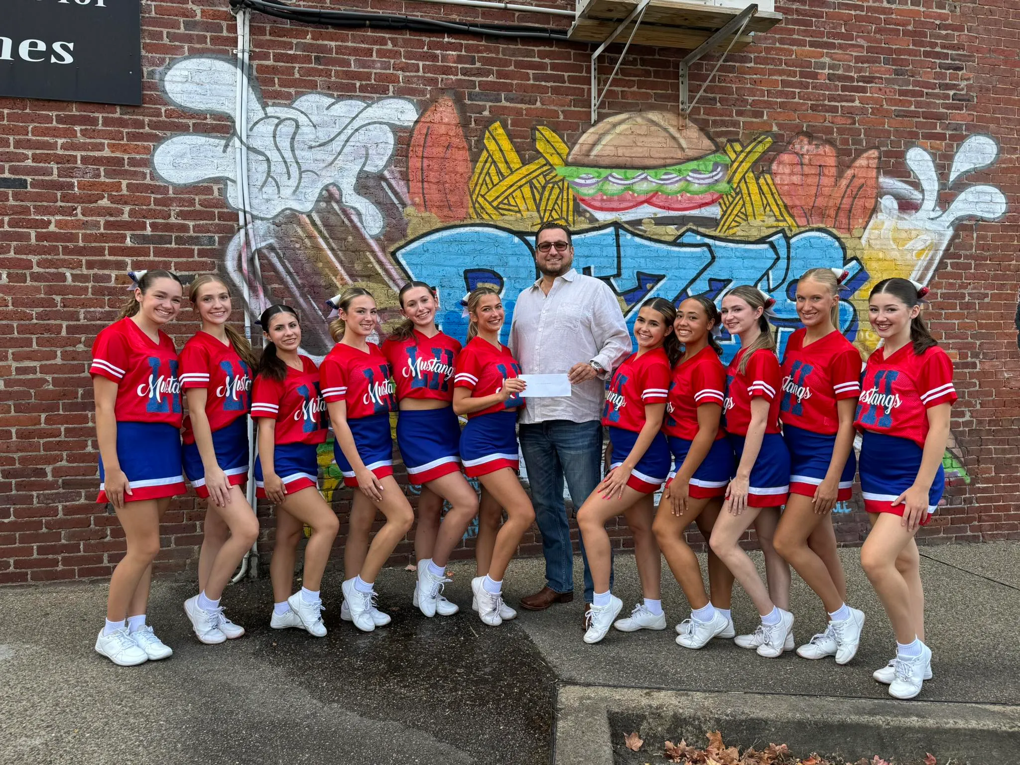The Laurel Highlands HS Mustangs cheer team in front of the Rizz's mural, accepting a sponsor check from Ben