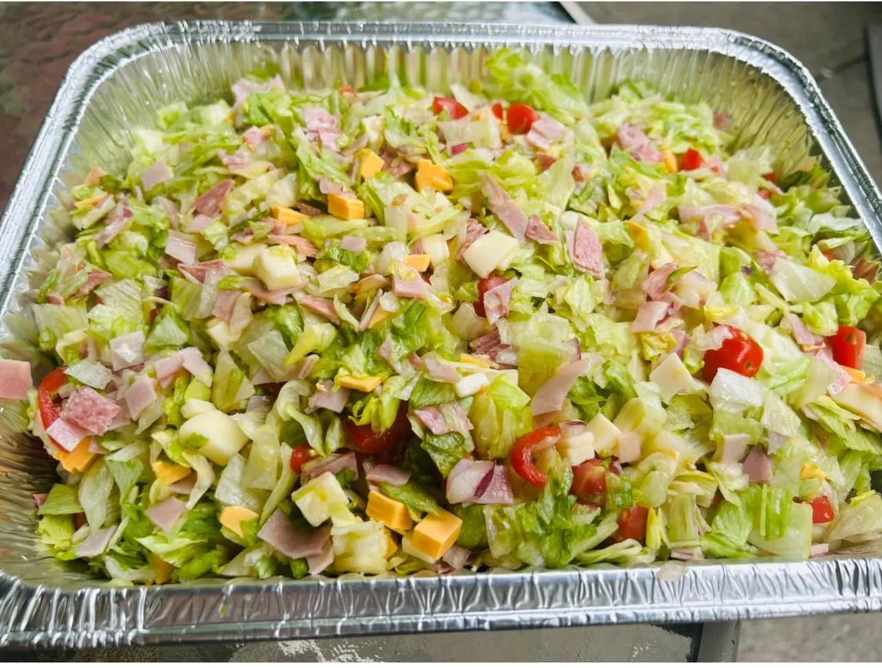 A full catering tray of Rizz's antipasto chopped salad — salami, ham, provolone, lettuce, tomato